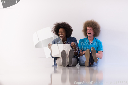 Image of multiethnic couple sitting on the floor with a laptop and tablet
