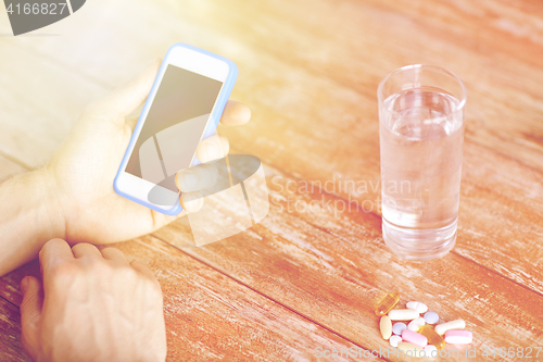 Image of close up of hands with smartphone, pills and water