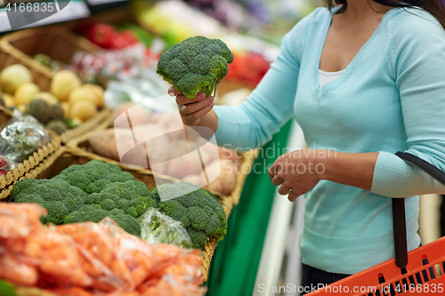 Image of woman with basket buying broccoli at grocery store