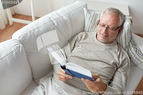 Image of senior man lying on sofa and reading book at home