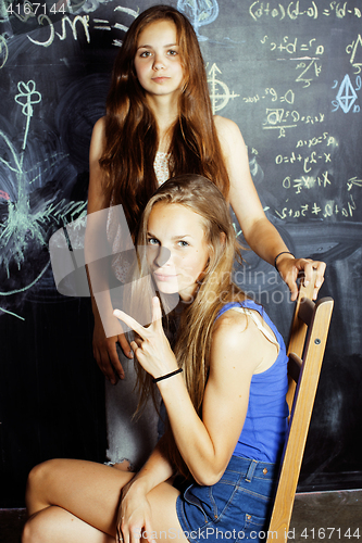 Image of back to school after summer vacations, two teen girls in classroom with blackboard painted together