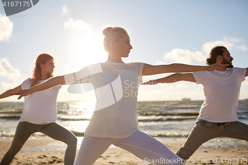 Image of group of people making yoga exercises on beach