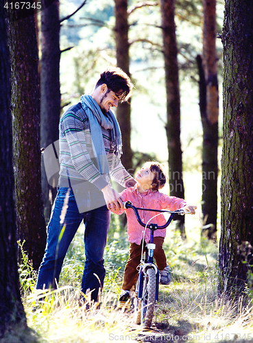 Image of father learning his son to ride on bicycle outside in park