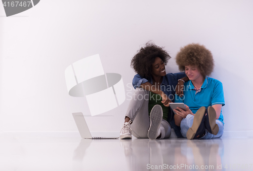 Image of multiethnic couple sitting on the floor with a laptop and tablet
