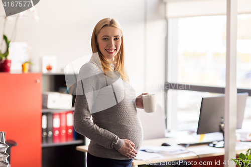 Image of pregnant businesswoman with cup of tea at office