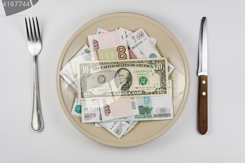 Image of On the plate is a lot of money Russian rubles, they have a ten dollars banknote, lie next to utensils top view