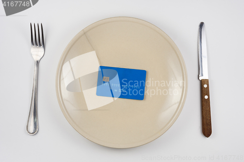 Image of On the cracked plate is a plastic credit card, next lie fork and knife, white background, top view