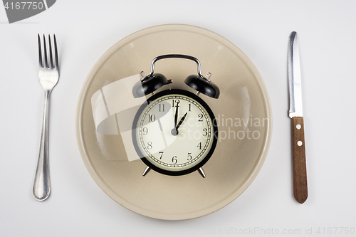 Image of On the plate is an alarm clock, lying next to a knife and fork, white background, top view