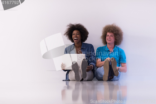 Image of multiethnic couple sitting on the floor with a laptop and tablet