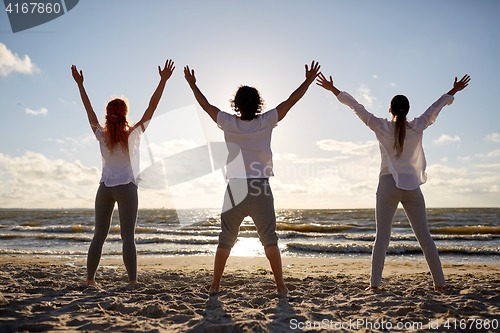 Image of group of people making yoga or meditating on beach