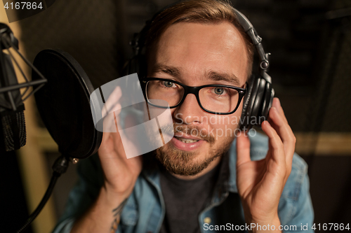 Image of man with headphones singing at recording studio