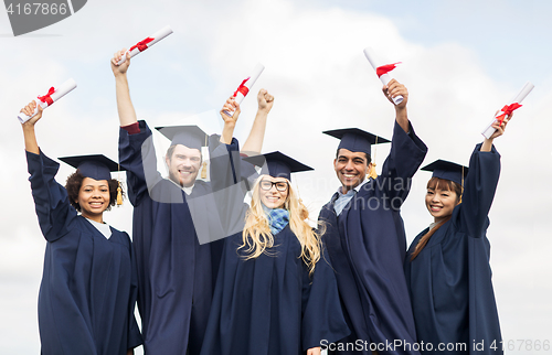 Image of happy students in mortar boards waving diplomas