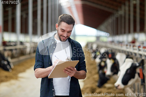 Image of farmer with clipboard and cows in cowshed on farm