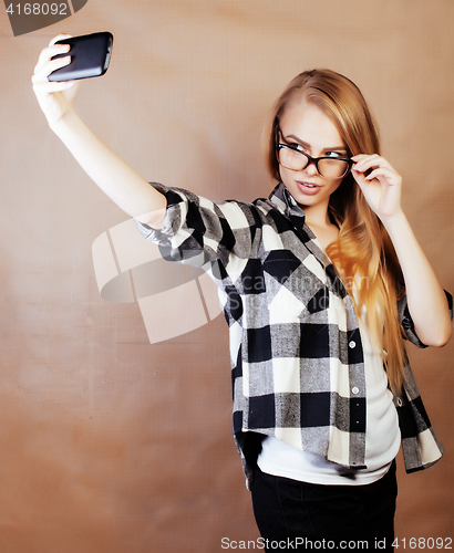 Image of young pretty blond hipster girl making selfie on warm brown back