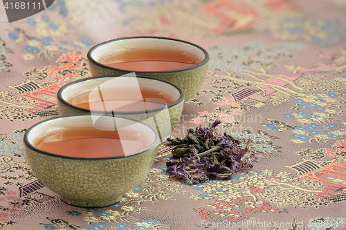 Image of  three cups filled with tea on a beautiful tablecloth