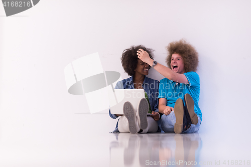 Image of multiethnic couple sitting on the floor with a laptop and tablet