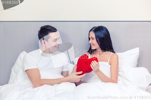 Image of smiling couple in bed with red heart shape pillow