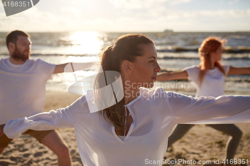 Image of group of people making yoga exercises on beach