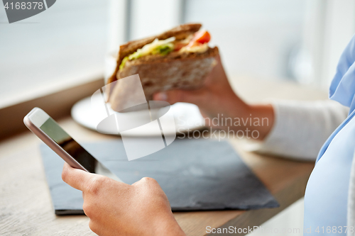 Image of woman with smartphone and sandwich at restaurant