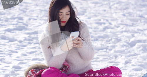 Image of Young woman sat on snow texting on mobile