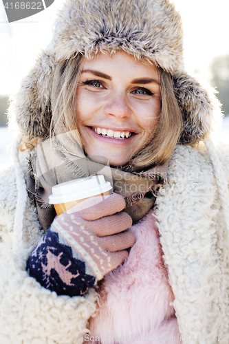 Image of young pretty teenage hipster girl outdoor in winter snow park having fun drinking coffee, warming up happy smiling, lifestyle people concept