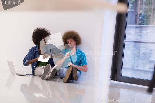 Image of multiethnic couple sitting on the floor with a laptop and tablet