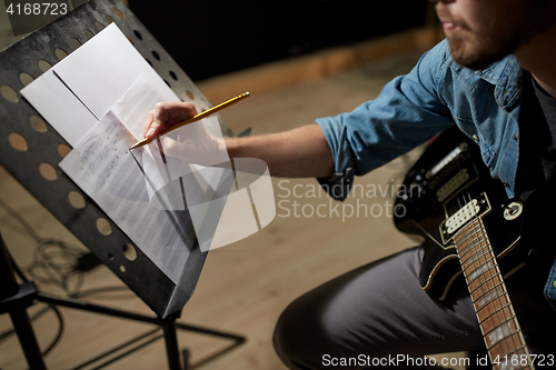 Image of man with guitar writing to music book at studio