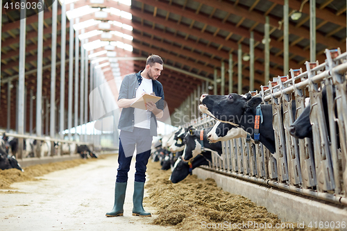 Image of farmer with clipboard and cows in cowshed on farm