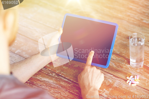 Image of close up of hands with tablet pc, pills and water