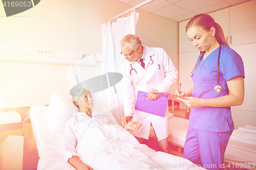 Image of doctor and nurse visiting senior woman at hospital