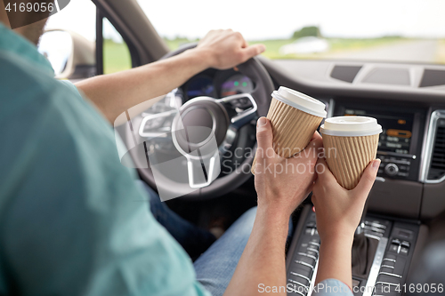 Image of close up of couple driving in car with coffee cups