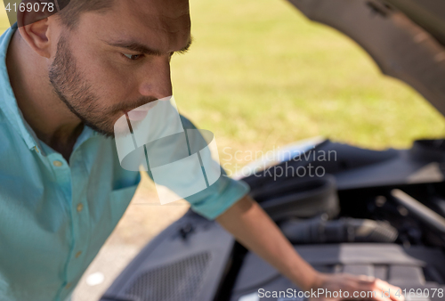 Image of man with open hood of broken car at countryside