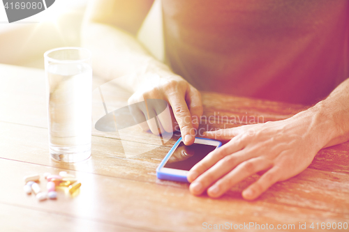 Image of close up of hands with smartphone, pills and water