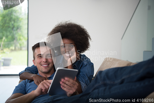 Image of multiethnic couple relaxing at  home with tablet computers