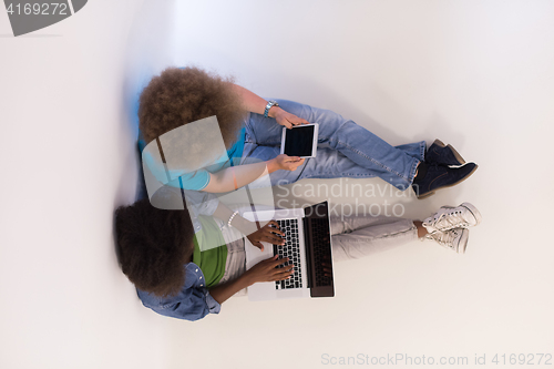 Image of multiethnic couple sitting on the floor with a laptop and tablet