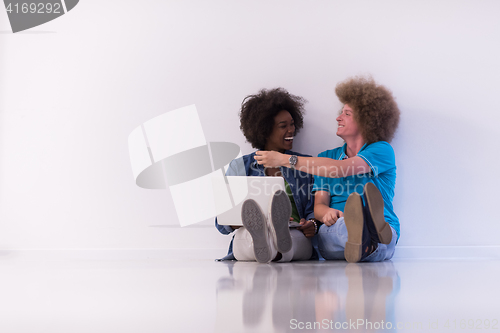 Image of multiethnic couple sitting on the floor with a laptop and tablet