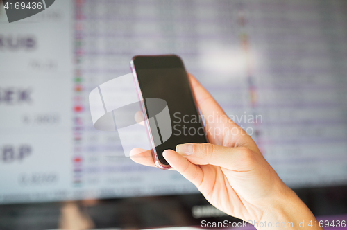 Image of hand with smartphone over exchange rates on screen