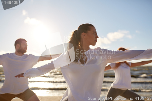 Image of group of people making yoga exercises on beach