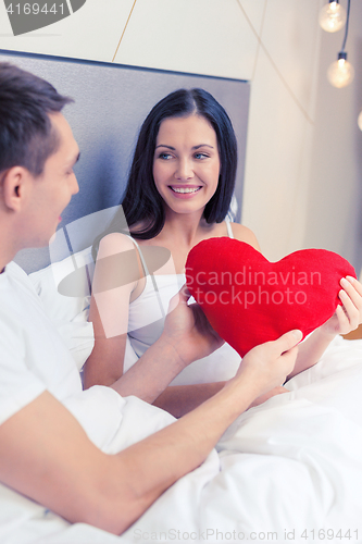 Image of smiling couple in bed with red heart shape pillow
