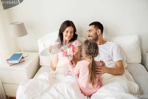 Image of happy girl giving flowers to mother in bed at home