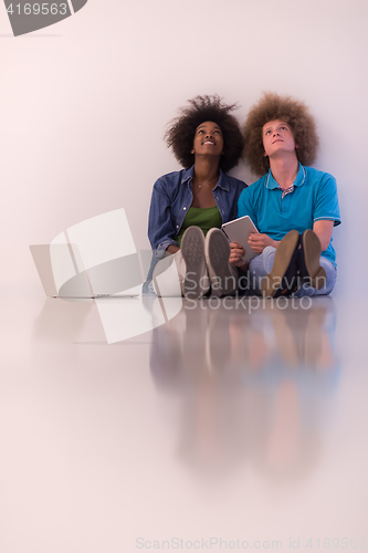 Image of multiethnic couple sitting on the floor with a laptop and tablet