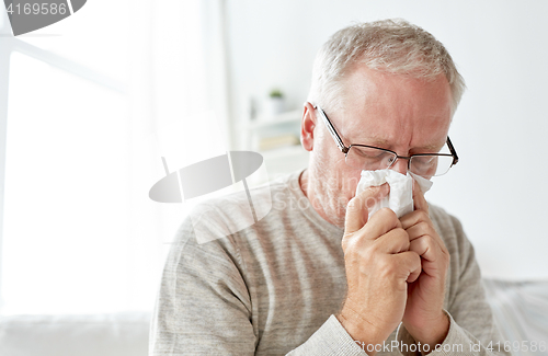 Image of sick senior man with paper wipe blowing his nose