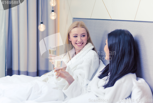 Image of smiling girlfriends with champagne glasses in bed