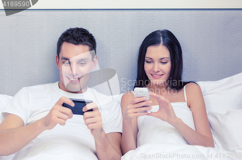 Image of smiling couple in bed with smartphones