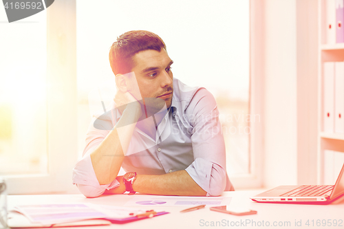 Image of bored businessman with laptop and papers at office