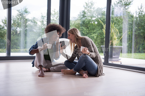 Image of multiethnic women sit on the floor and drinking coffee
