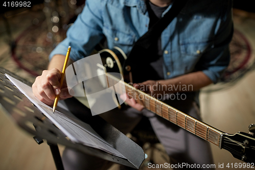 Image of man with guitar writing to music book at studio