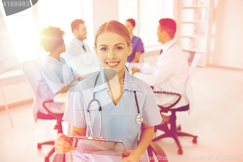 Image of happy doctor with clipboard over group of medics