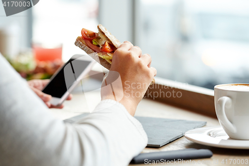 Image of woman with smartphone and sandwich at restaurant