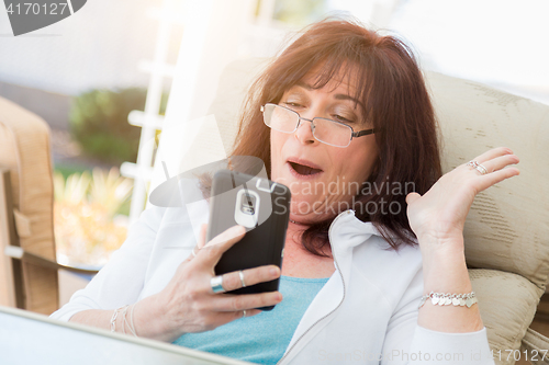 Image of Shocked Middle Aged Woman Gasps While Using Her Smart Phone